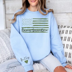 May include: Light blue sweatshirt with a green and white American flag design and the text "Army Grandma" and "Billy" with a green heart.