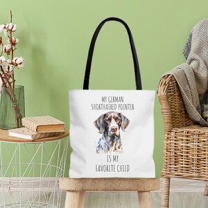 May include: White tote bag with black handles featuring a watercolor illustration of a German Shorthaired Pointer dog. The text on the bag reads "My German Shorthaired Pointer is my favorite child."