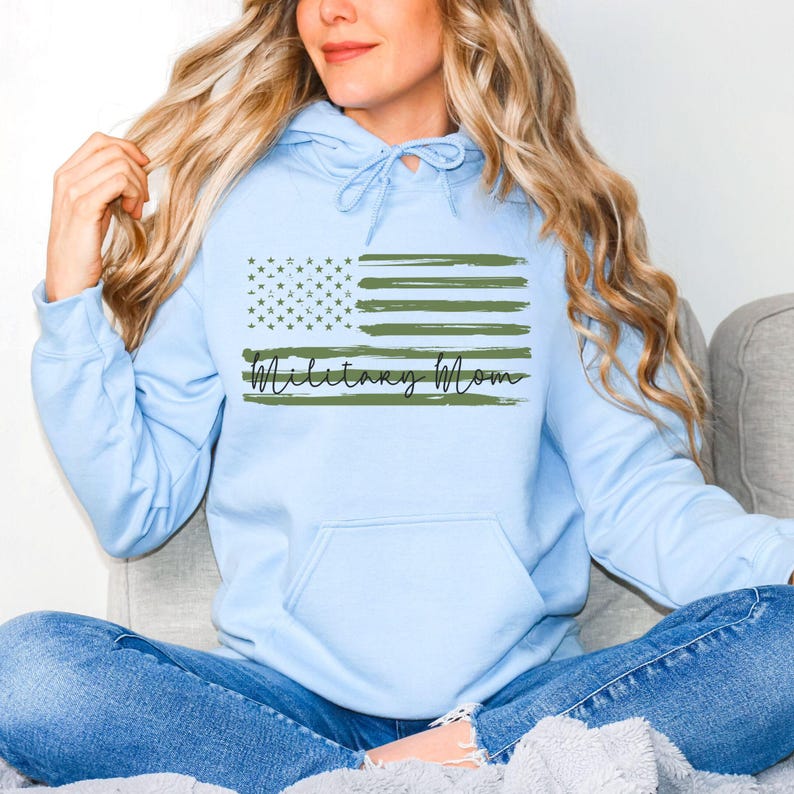 May include: A light blue hooded sweatshirt with a green camouflage American flag and the text "Military Mom" printed on the front.