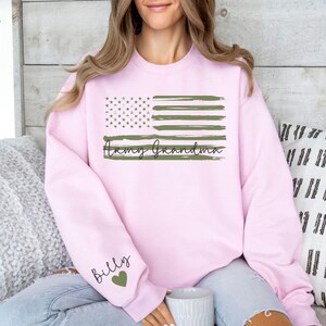 May include: Pink sweatshirt with a green and white American flag design and the text "Army Grandma". The left sleeve has the name "Billy" and a green heart.