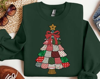 Può includere: Una felpa verde scuro con un design a forma di albero di Natale. L'albero è composto da toppe fantasia rosse, verdi e bianche, sormontato da una stella dorata e un fiocco rosso. La felpa ha un girocollo e maniche lunghe.