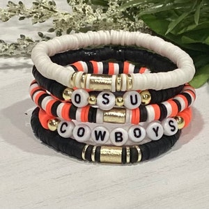 May include: A set of five bracelets with black, white, and orange beads. The bracelets spell out "OSU COWBOYS".