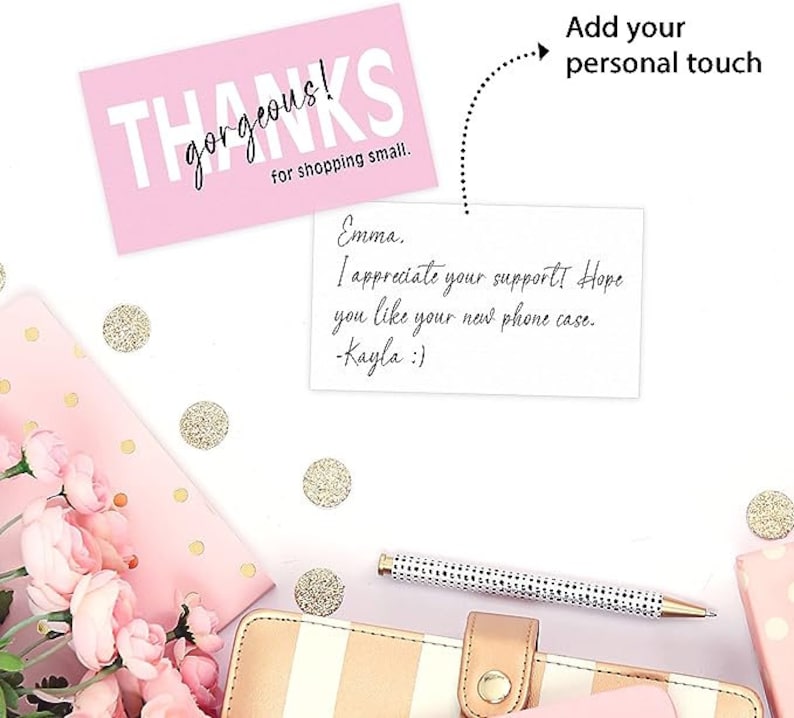以下が含まれることがあります： ピンクのサンキューカードに「THANKS gorgeous! for shopping small.」というテキストと、「Emma. I appreciate your support! Hope you like your new phone case. -Kayla :)」という手書きのメモが書かれています