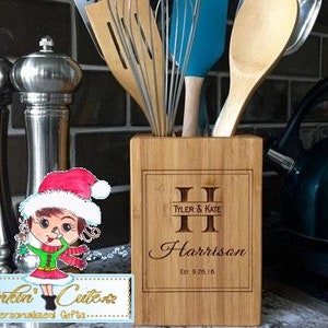May include: Personalized bamboo kitchen utensil holder with the names Tyler & Kate Harrison and the date Est. 9.26.16 engraved on the front. The holder is filled with various kitchen utensils, including a wooden spoon, a blue whisk, and a wooden spatula.