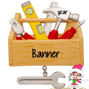 May include: A wooden toolbox Christmas ornament with a hammer, screwdriver, pliers, and level. The toolbox has the word "Banner" written on the front. A silver wrench hangs from the bottom of the ornament.