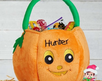 May include: A plush orange pumpkin-shaped treat basket with a bright green handle and a green leaf accent. The front features an embroidered jack-o'-lantern face and the name Hunter in black thread. The basket is filled with assorted candy.