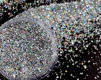 Könnte beinhalten: Ein klares Glas gefüllt mit schimmerndem silbernem Glitter. Der Glitter ist auf einer schwarzen Oberfläche verstreut.