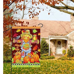 May include: A fall-themed garden flag featuring a scarecrow, pumpkins, and the text "Happy Fall y'all." The flag has a burgundy background with colorful autumn leaves and a green border. The flag is displayed in a yard with a house in the background.