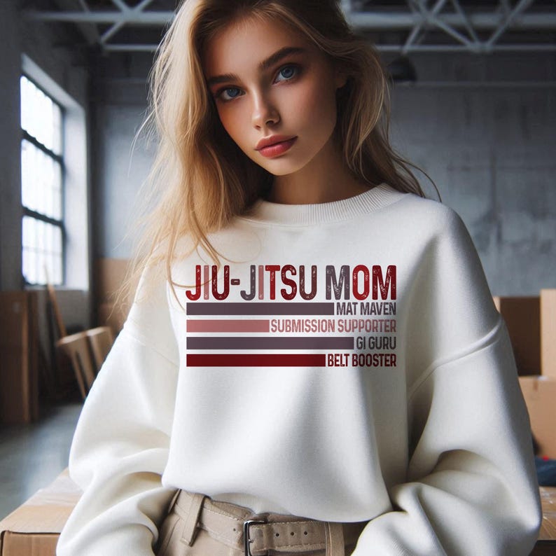 May include: White sweatshirt with the text "Jiu-Jitsu Mom" in red and brown. The text is layered with the words "Mat Maven", "Submission Supporter", "Gi Guru", and "Belt Booster" underneath.