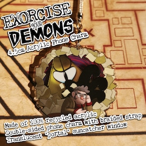 May include: A 4.5 inch double-sided acrylic phone charm featuring a cartoon character with a golden pyramid and the text "Exorcise Your Demons". The charm is translucent and has a braided strap.