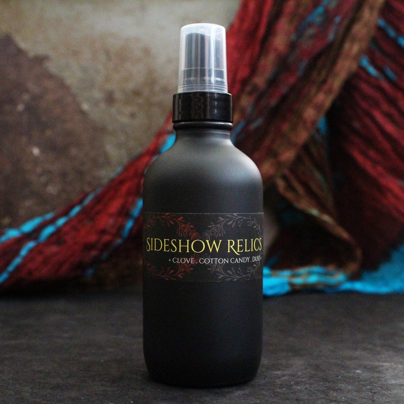 May include: A black glass bottle with a black spray nozzle and a label that reads "Sideshow Relics - Clove, Cotton Candy, Dust".