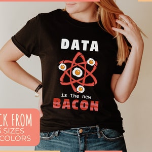 May include: Black t-shirt with the text "DATA is the new BACON" in white and red. The design features an atom model made of bacon and eggs. The shirt also has the text "PICK FROM 6 SIZES 12 COLORS".