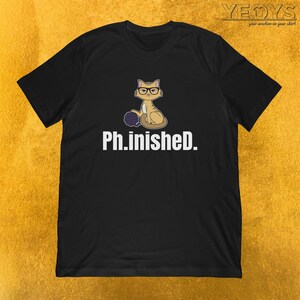 May include: Black t-shirt featuring a cartoon cat wearing glasses and holding a ball of yarn. The text "Ph.inished." is below the cat.