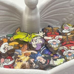 May include: A collection of colorful acrylic character charms featuring Snow White and the Seven Dwarfs, resting inside a white, 3D-printed butterfly-shaped dish. The charms depict various figures in vibrant outfits, including yellow, red, and blue, with detailed facial expressions and distinct poses.