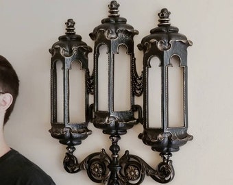 May include: A black metal wall sconce with three ornate candle holders. The sconce has a decorative scrollwork design and a black finish.