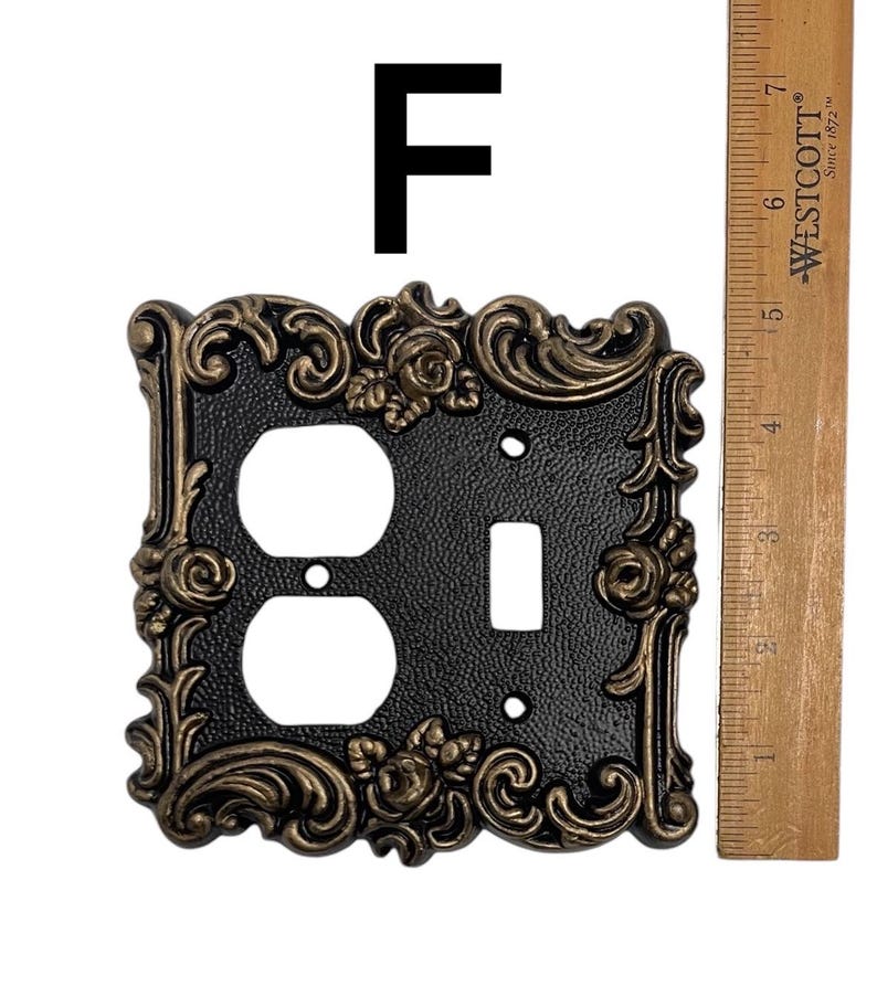 May include: A black and gold decorative outlet and light switch cover with a floral design. The cover is approximately 4 inches tall and 3 inches wide.