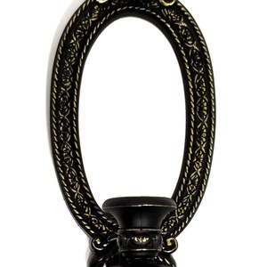 May include: Black and gold oval wall sconce with a candle holder. The sconce has a decorative design with a floral motif.
