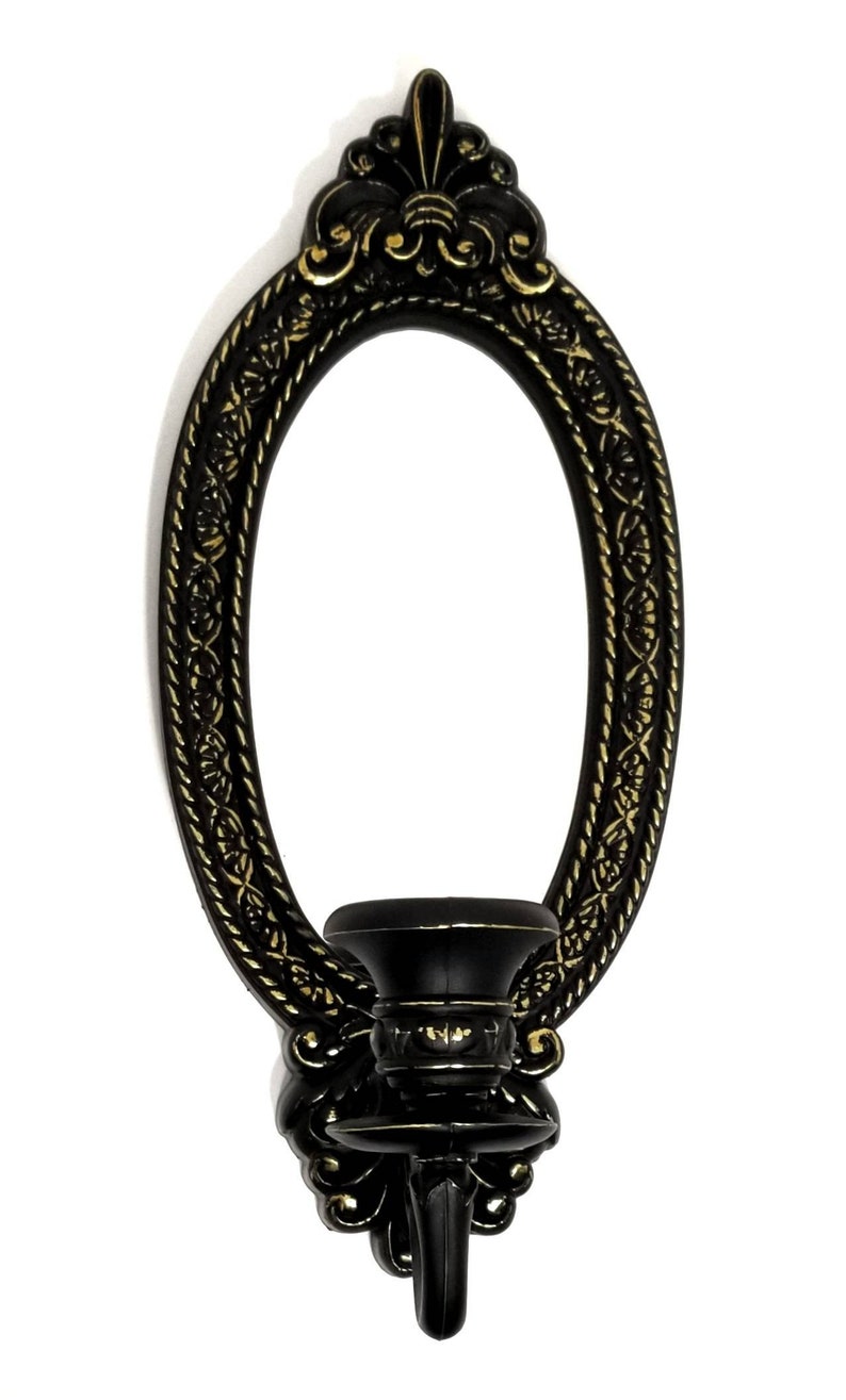 May include: Black and gold oval wall sconce with a candle holder. The sconce has a decorative design with a floral motif.