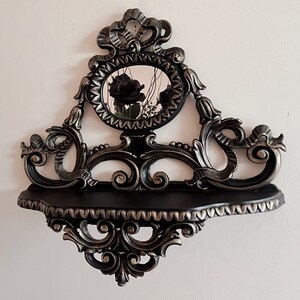 May include: Black and silver ornate shelf with a decorative mirror featuring black roses. The shelf has a scrolled design and a scalloped edge.