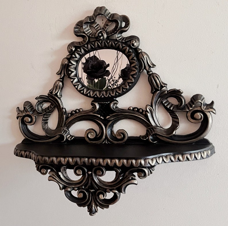 May include: Black and silver ornate shelf with a decorative mirror featuring black roses. The shelf has a scrolled design and a scalloped edge.