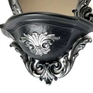 May include: Black wall shelf with ornate silver detailing. The shelf has a curved, bowl-like shape and is designed to be mounted on a wall.