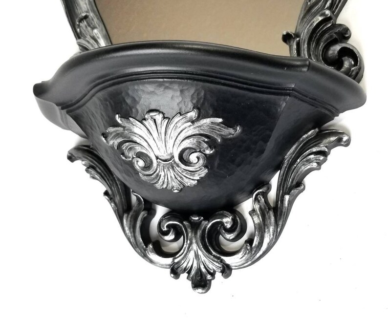 May include: Black wall shelf with ornate silver detailing. The shelf has a curved, bowl-like shape and is designed to be mounted on a wall.