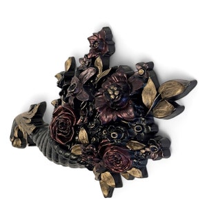 Puede incluir: Una cornucopia negra rebosante de flores burdeos, rojas y doradas. La cornucopia es una decoraci&oacute;n de pared con un dise&ntilde;o floral en 3D.