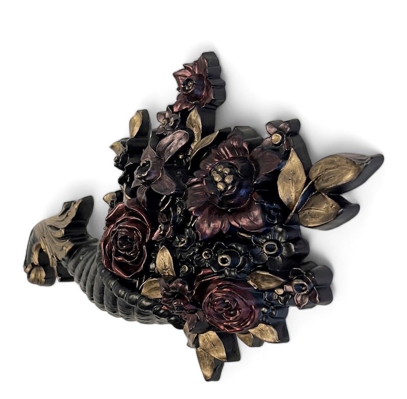 Puede incluir: Una cornucopia negra rebosante de flores burdeos, rojas y doradas. La cornucopia es una decoraci&oacute;n de pared con un dise&ntilde;o floral en 3D.