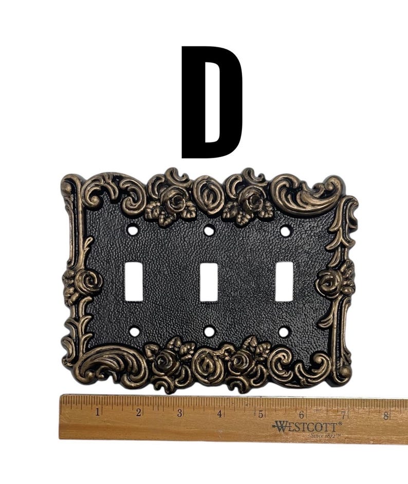 May include: A black light switch plate with a gold ornate frame featuring floral designs. The plate has three toggle switches.