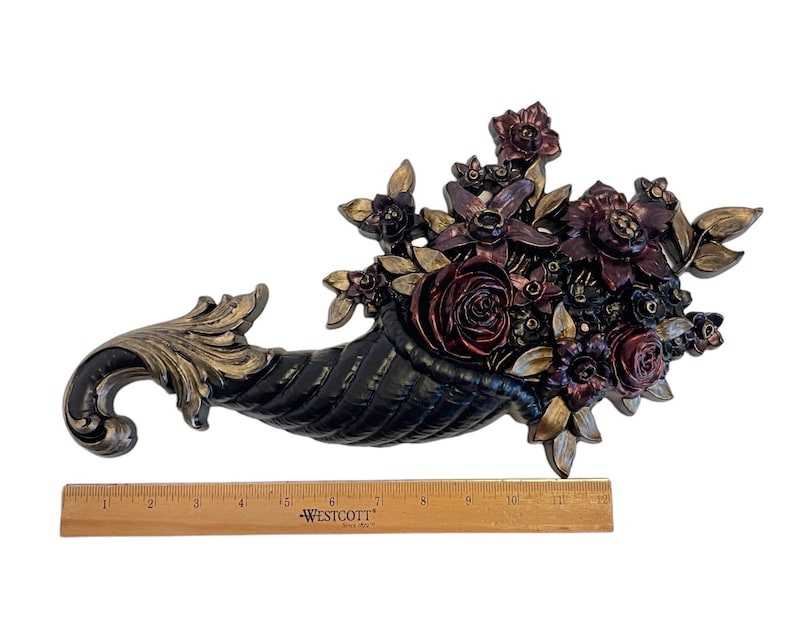 Puede incluir: Una cornucopia negra rebosante de flores burdeos, rojas y doradas. La cornucopia est&aacute; hecha de un material texturizado y tiene un acabado dorado. Las flores est&aacute;n dispuestas en un estilo realista y tienen un toque vintage.