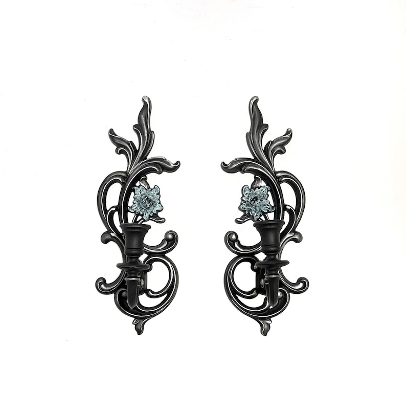 May include: A pair of black metal wall sconces with ornate scrollwork and a floral design. Each sconce features a clear glass flower with a blue centre.