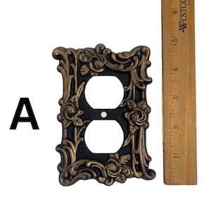 May include: A black and gold decorative outlet cover with a floral design. The cover is approximately 4 inches tall and 3 inches wide.