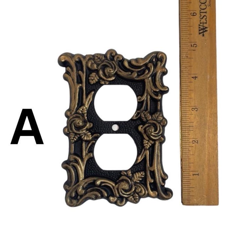 May include: A black and gold decorative outlet cover with a floral design. The cover is approximately 4 inches tall and 3 inches wide.