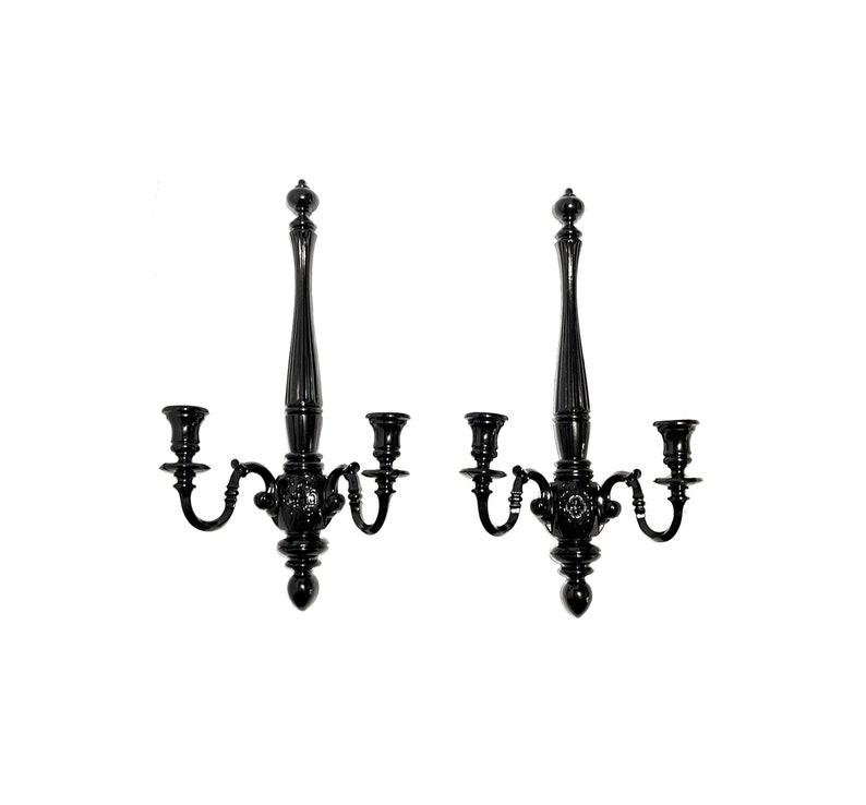 Op de afbeelding: Een paar zwarte metalen wandkandelaars met elk drie kaarsarmen. De kandelaars hebben een decoratief, versierd ontwerp.