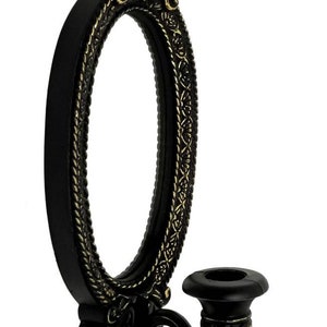 May include: Black oval wall mirror with ornate gold accents and a single candle holder attached to the side.