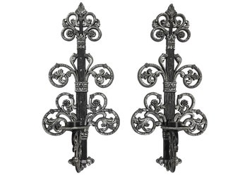 Op de afbeelding: Een paar zwarte metalen wandlampen met sierlijke krulwerk en kaarshouders.