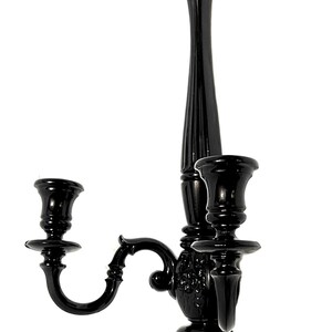 Op de afbeelding: Zwarte metalen wandkandelaar met twee armen en een decoratief ontwerp. De kandelaar heeft een hoge, slanke basis en twee gebogen armen die elk een kaarshouder dragen.