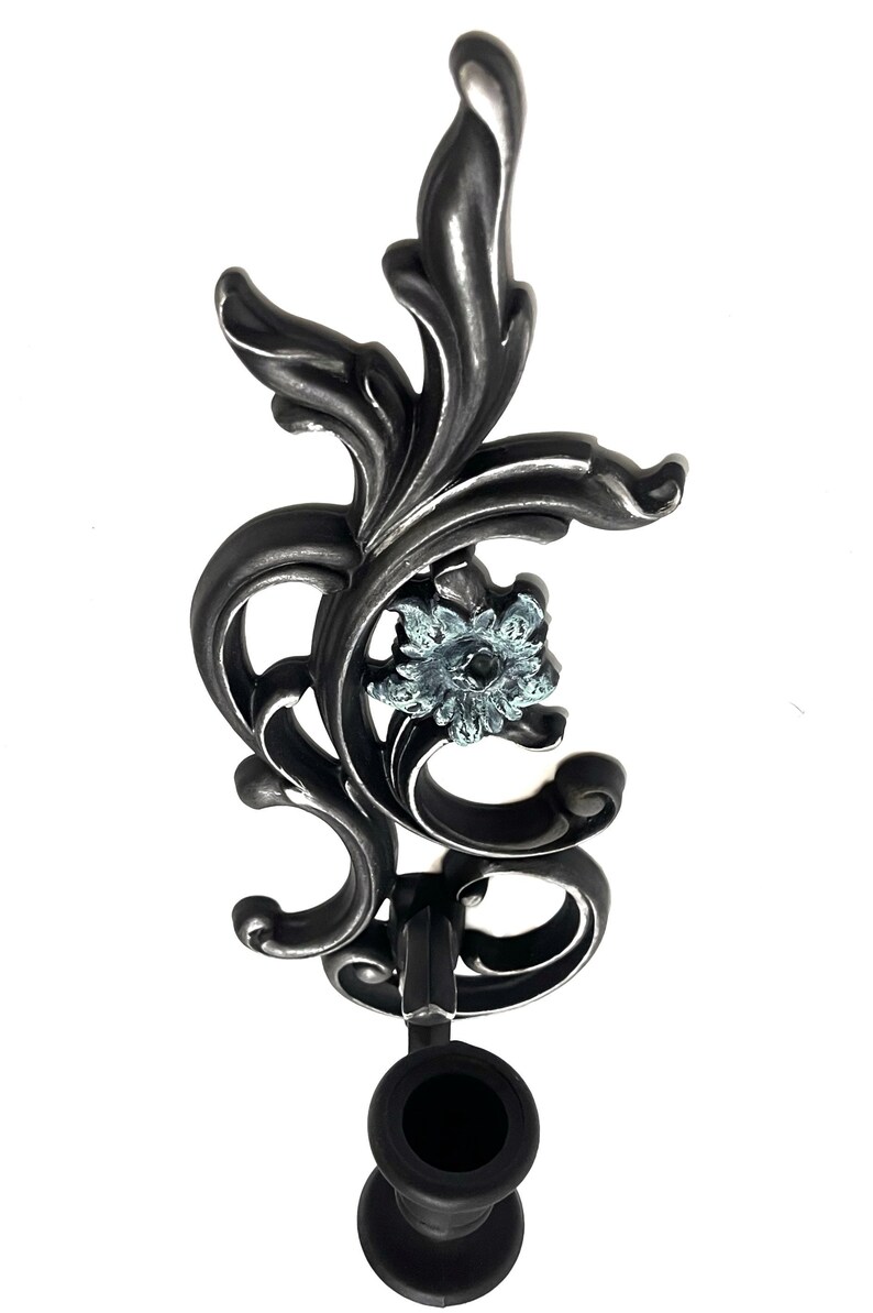 May include: A black metal candle holder with a decorative floral design and a blue glass flower accent. The holder has a black rubber base.