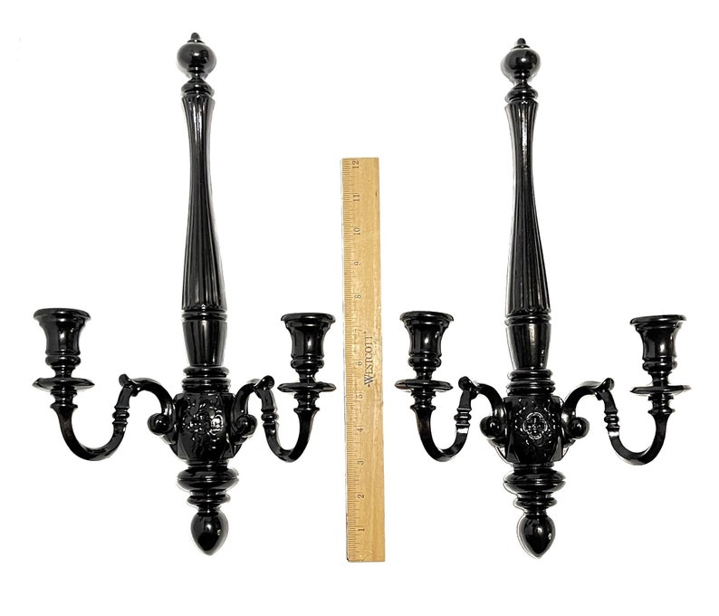 Op de afbeelding: Een paar zwarte metalen wandkandelaars met elk drie kaarsarmen. De kandelaars zijn versierd en hebben een decoratief ontwerp.