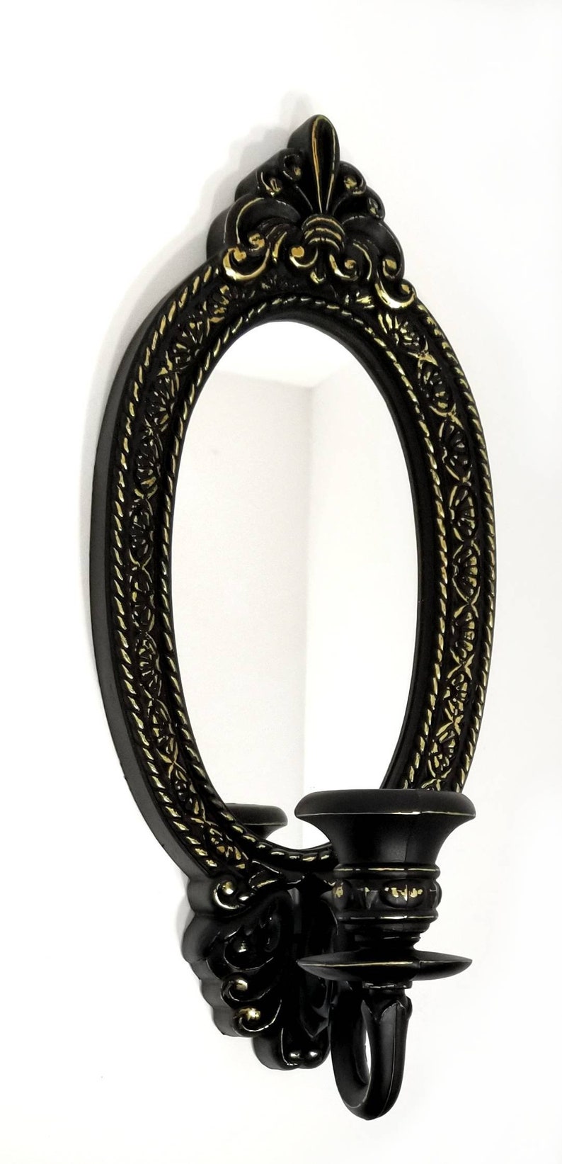 May include: Black oval mirror with a gold ornate frame and a single candle holder on the side. The mirror has a simple design and the candle holder is ornate.
