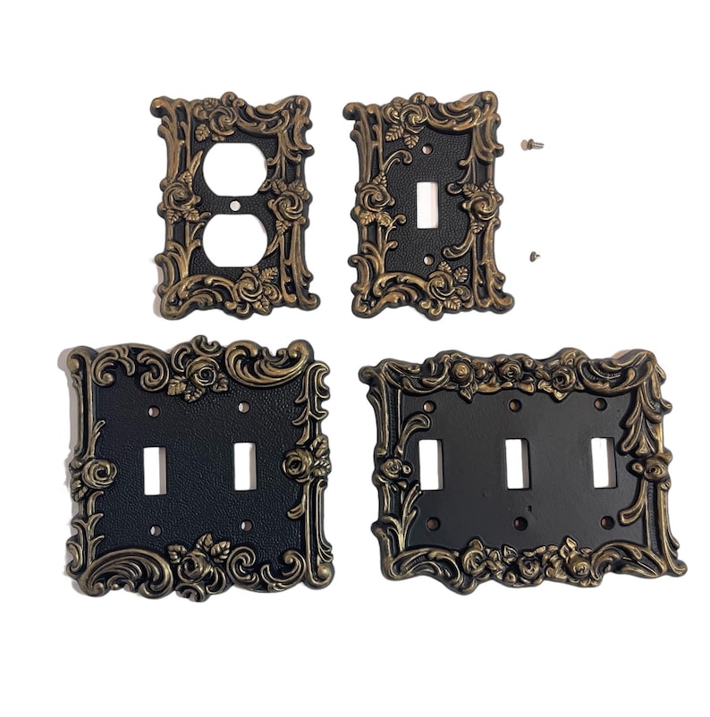 May include: Set of four decorative light switch plates with ornate gold-colored frames and black inserts. The plates feature a floral design with roses and scrolls.