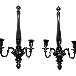 Op de afbeelding: Een paar zwarte metalen wandkandelaars met elk drie kaarsarmen. De kandelaars hebben een decoratief, versierd ontwerp.