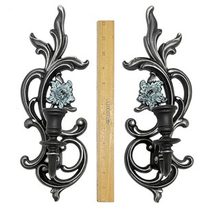 May include: A pair of silver metal wall sconces with a floral design and a blue glass flower accent. Each sconce has a candle holder.