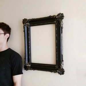 May include: A black ornate picture frame with a gold-toned finish. The frame has a decorative design with intricate details.