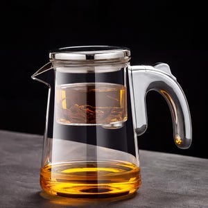 May include: A clear glass teapot with a stainless steel handle and lid. The teapot contains brewed tea, with a separate infuser basket holding loose tea leaves. The tea has a golden-yellow hue.