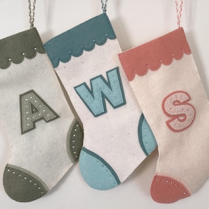 May include: Three felt Christmas stockings with the letters A, W, and S embroidered on them. The stockings are in shades of green, blue, and pink.