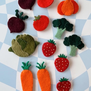 May include: Felt food set with various fruits and vegetables, including red and green apples, carrots, strawberries, tomatoes, and broccoli. The felt pieces are colorful and detailed.