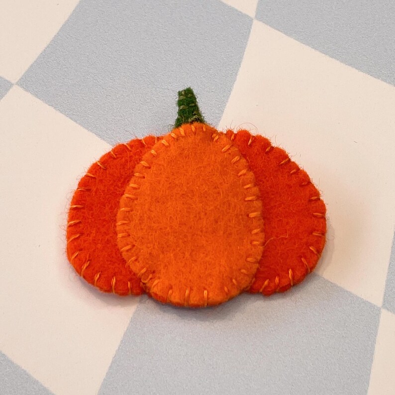 May include: A felt pumpkin ornament with three layers, featuring a green stem and orange felt.
