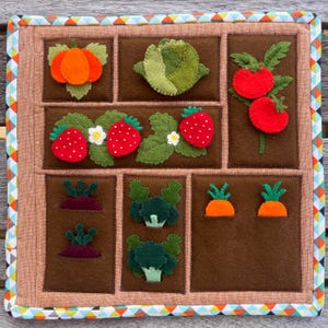 Puede incluir: Una alfombra de juego de jardín de fieltro con varias verduras y frutas, incluyendo una calabaza, col, tomates, fresas, zanahorias y brócoli. La alfombra es marrón con un borde marrón claro y un ribete de patrones coloridos.