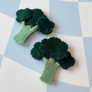 May include: Two felt broccoli ornaments, one green and one dark green, with a light green stem.